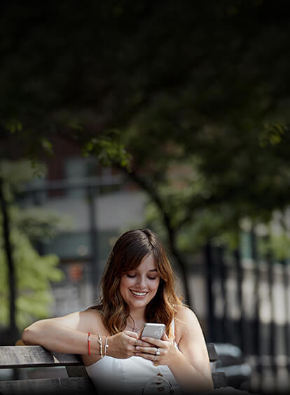 Mujer joven disfrutando de su teléfono 5G en un banco de plaza.