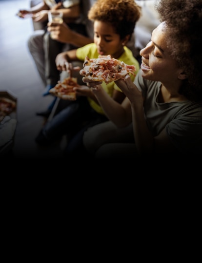Mujer y su niño sonriendo mientras comen pizza.